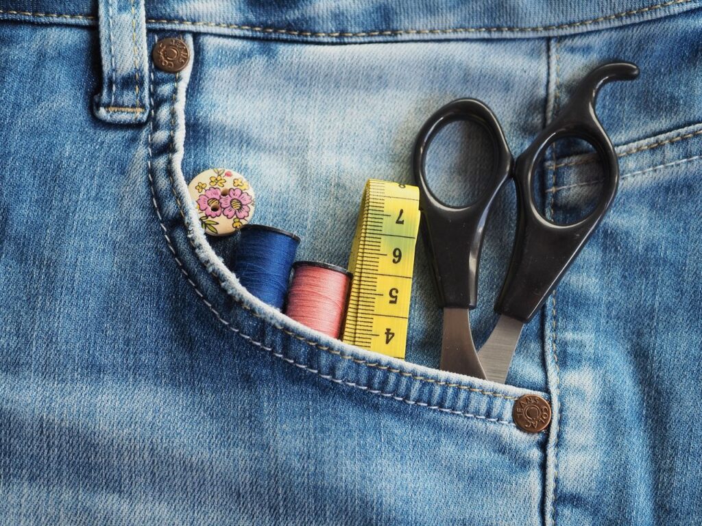 Close-up of sewing accessories in a denim pocket, featuring threads, scissors, and measuring tape.