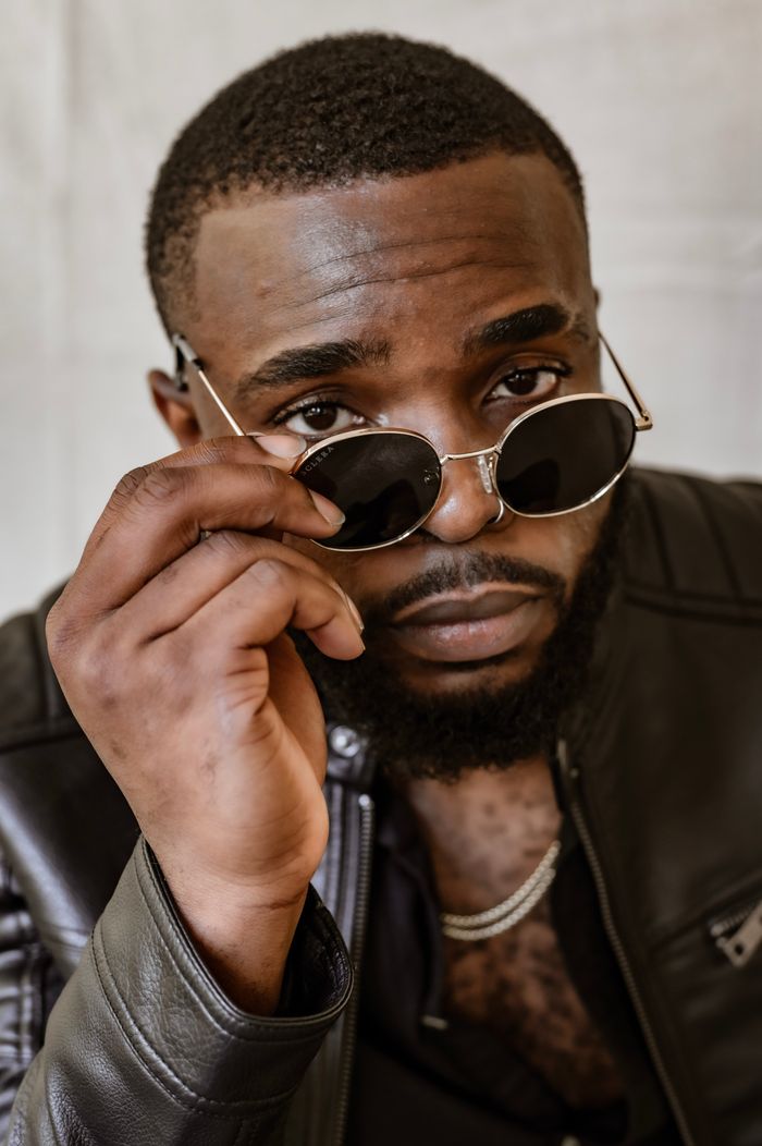 Confident man posing with sunglasses, wearing a leather jacket in a close-up portrait.